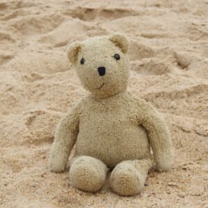 A lone teddy bear sits on a sandy beach, evoking nostalgia and childhood memories.