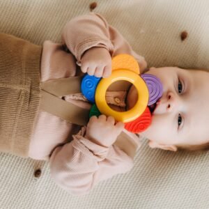 Cute baby chewing on a colorful teething toy while lying on a soft surface.