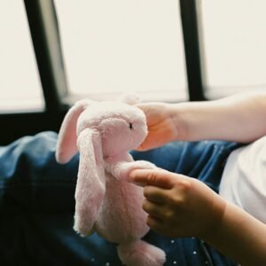 A cozy moment of a child holding a pink plush bunny toy by the window, conveying comfort and warmth.