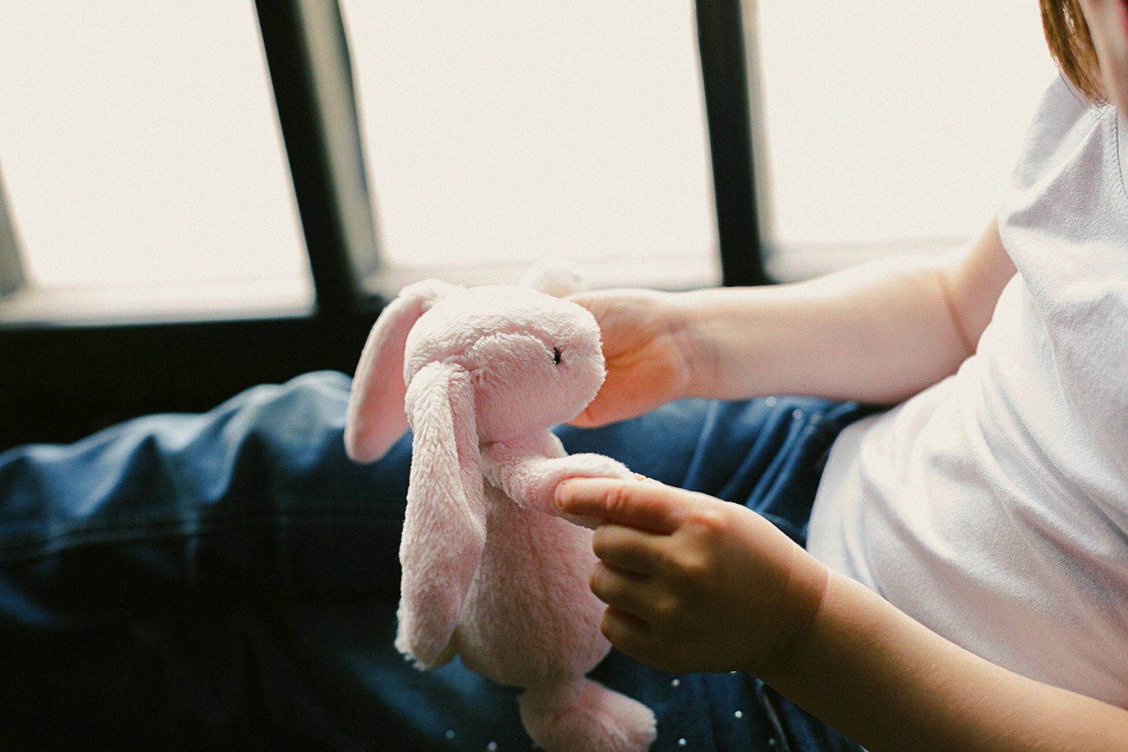 A cozy moment of a child holding a pink plush bunny toy by the window, conveying comfort and warmth.
