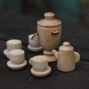 A close-up view of a miniature wooden tea set featuring a samovar, cups, and a kettle on a dark surface.