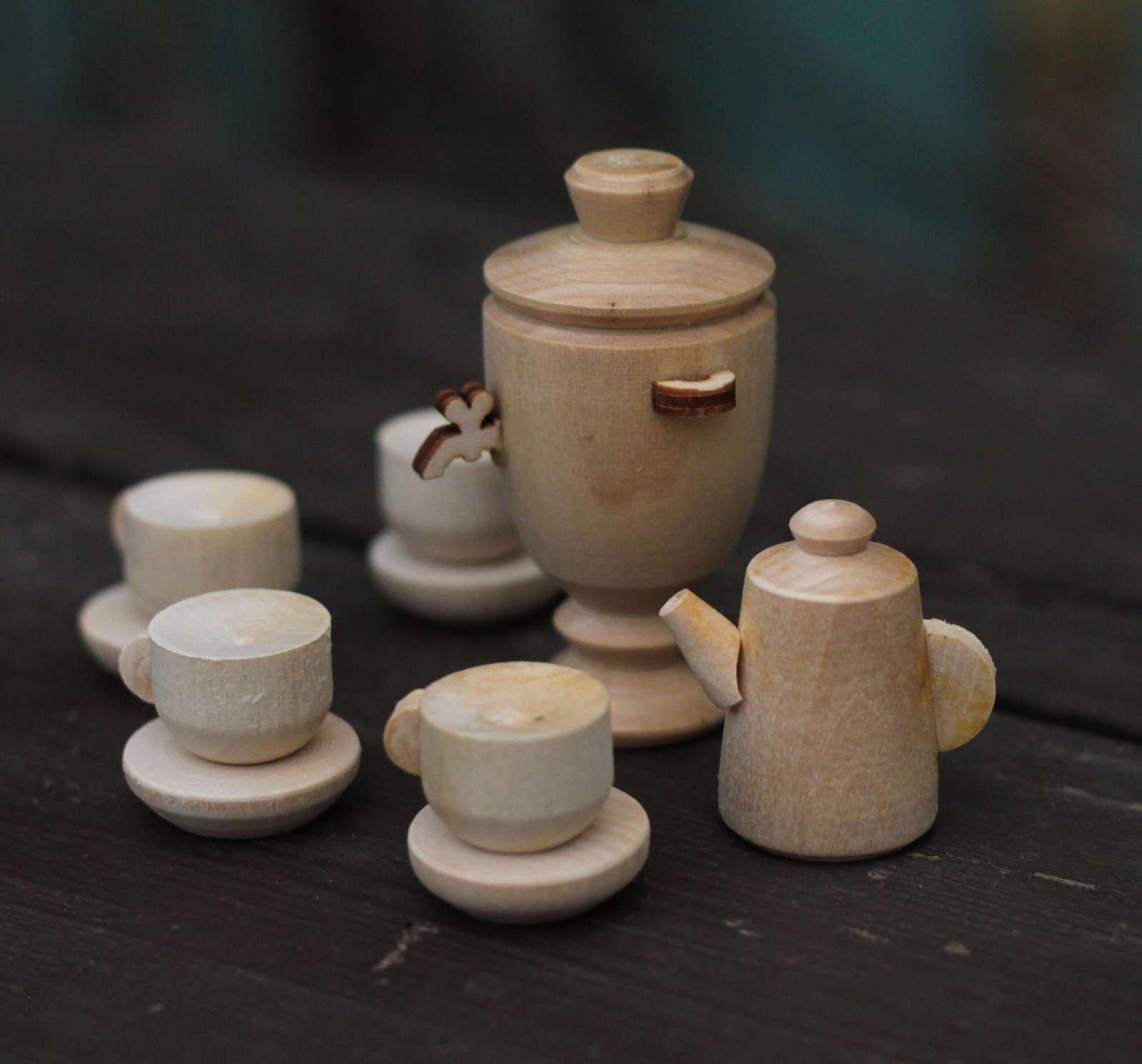 A close-up view of a miniature wooden tea set featuring a samovar, cups, and a kettle on a dark surface.